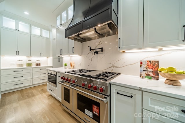 kitchen with double oven range, light stone countertops, white cabinetry, and custom range hood