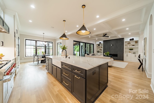 kitchen featuring coffered ceiling, hanging light fixtures, a large island with sink, beam ceiling, and sink