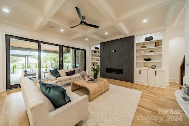 living room featuring a large fireplace, built in shelves, beamed ceiling, and light wood-type flooring