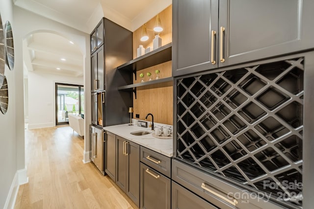 kitchen with ornamental molding, light hardwood / wood-style flooring, light stone counters, and sink