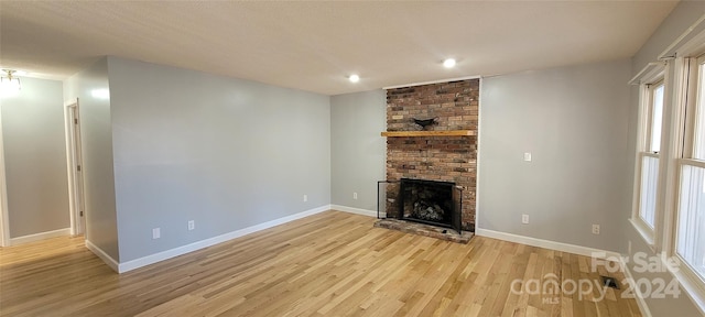 unfurnished living room with brick wall, light hardwood / wood-style flooring, and a brick fireplace