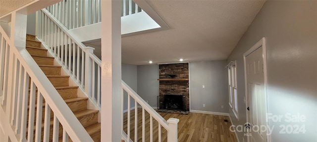 stairs with light hardwood / wood-style flooring, a fireplace, brick wall, and a textured ceiling