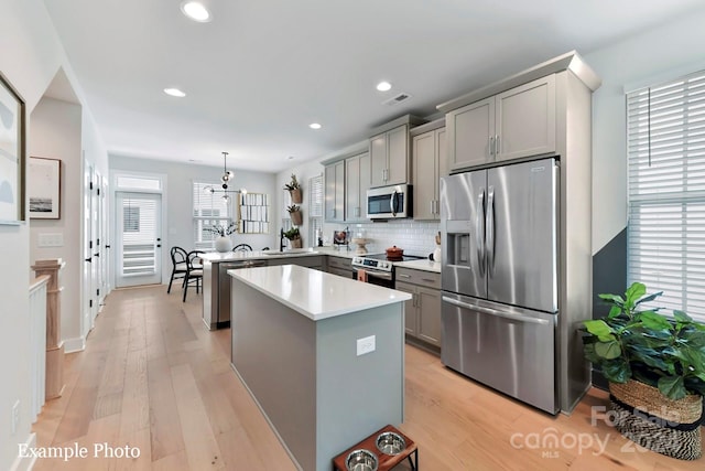 kitchen featuring hanging light fixtures, tasteful backsplash, stainless steel appliances, light hardwood / wood-style floors, and gray cabinets