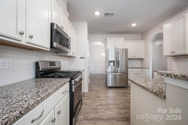 kitchen with appliances with stainless steel finishes, white cabinetry, backsplash, and hardwood / wood-style flooring