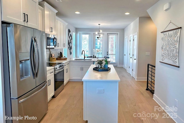 kitchen featuring sink, light hardwood / wood-style flooring, hanging light fixtures, stainless steel appliances, and white cabinets