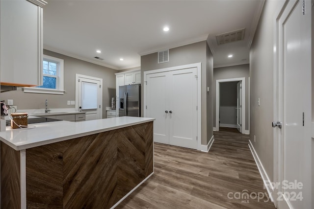 kitchen with kitchen peninsula, ornamental molding, white cabinets, stainless steel refrigerator with ice dispenser, and hardwood / wood-style flooring