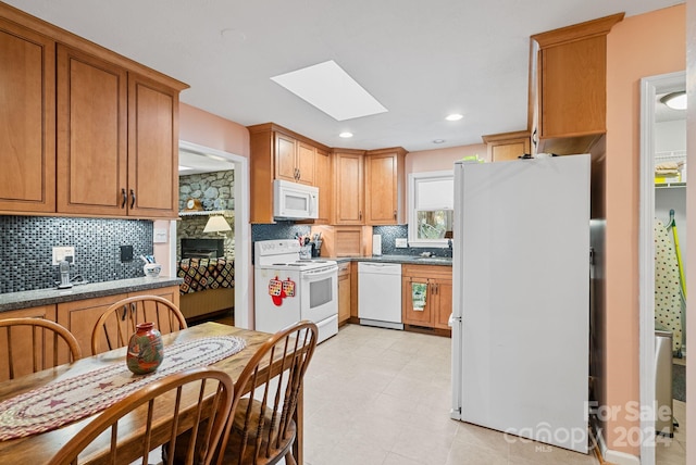 kitchen with a skylight, sink, white appliances, light tile flooring, and tasteful backsplash