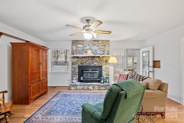 living room featuring light hardwood / wood-style floors, ceiling fan, a fireplace, and a textured ceiling