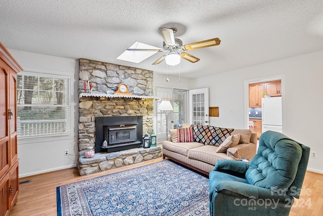 living room featuring a fireplace, light hardwood / wood-style flooring, a skylight, ceiling fan, and a textured ceiling