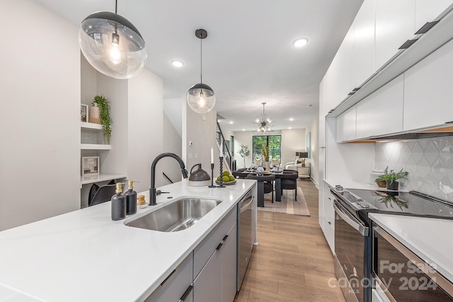 kitchen with decorative light fixtures, light hardwood / wood-style floors, stainless steel appliances, backsplash, and sink