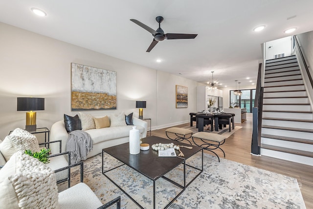 living room with ceiling fan with notable chandelier and light hardwood / wood-style floors