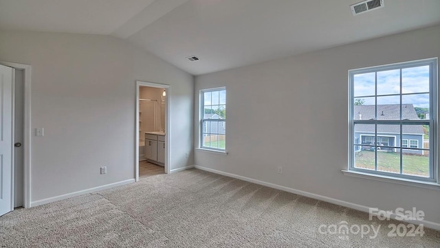 unfurnished bedroom with light colored carpet, ensuite bathroom, vaulted ceiling, and multiple windows