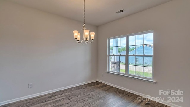 empty room with dark hardwood / wood-style floors and a notable chandelier