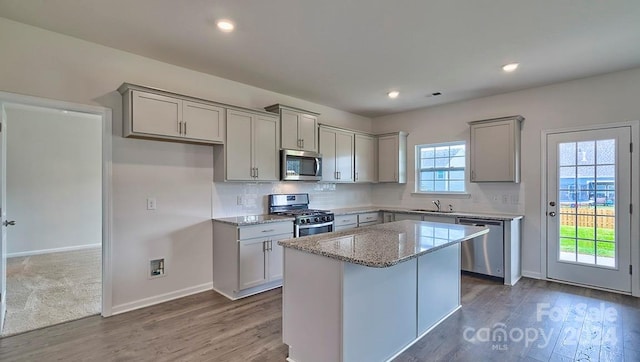 kitchen featuring sink, stainless steel appliances, light stone counters, a kitchen island, and gray cabinets