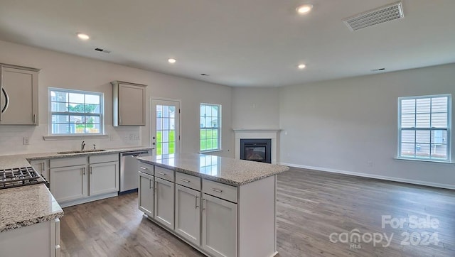 kitchen with a center island, dishwasher, light stone countertops, tasteful backsplash, and light wood-type flooring