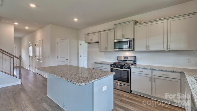 kitchen featuring backsplash, appliances with stainless steel finishes, light hardwood / wood-style floors, light stone counters, and a kitchen island