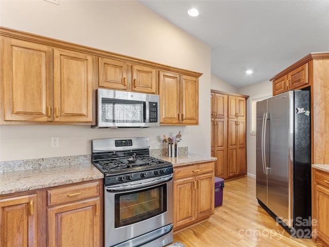 kitchen featuring lofted ceiling, light stone countertops, stainless steel appliances, and light hardwood / wood-style flooring