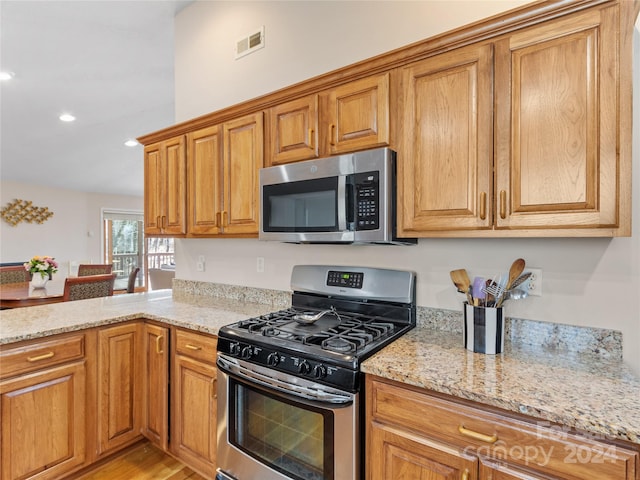 kitchen with appliances with stainless steel finishes, light hardwood / wood-style floors, and light stone countertops