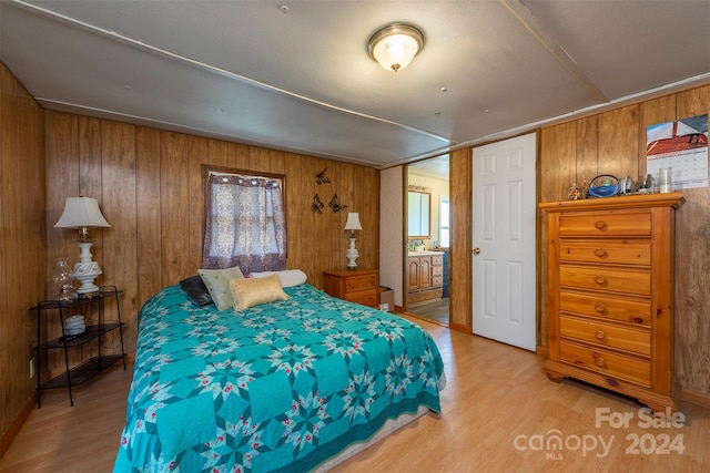 bedroom with wooden walls, light wood-type flooring, and ensuite bathroom