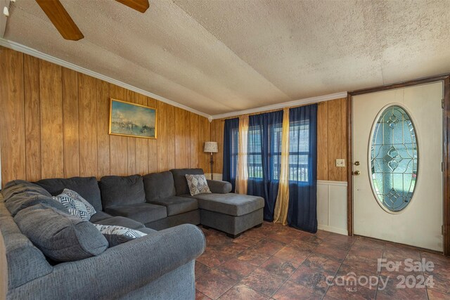 living room featuring ceiling fan, dark tile flooring, a textured ceiling, and wooden walls