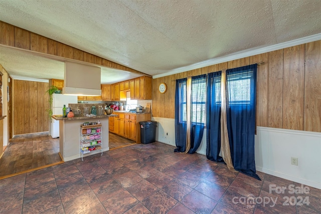 kitchen featuring dark hardwood / wood-style floors, wood walls, ornamental molding, and a textured ceiling