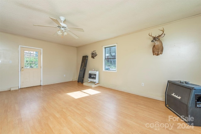 unfurnished room featuring ceiling fan, a textured ceiling, light wood-type flooring, and a wood stove