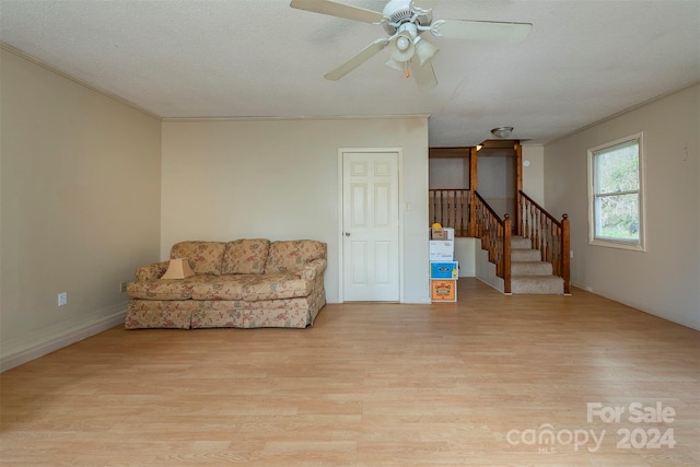 living area with a textured ceiling, ceiling fan, light wood-type flooring, and crown molding