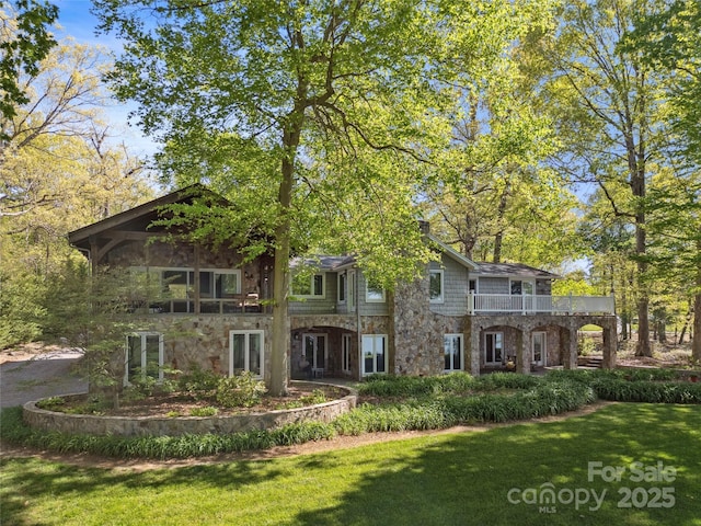 view of front of property with a balcony, stone siding, and a front lawn