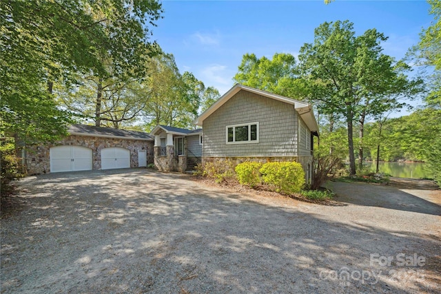 view of front of house featuring an attached garage, stone siding, and gravel driveway