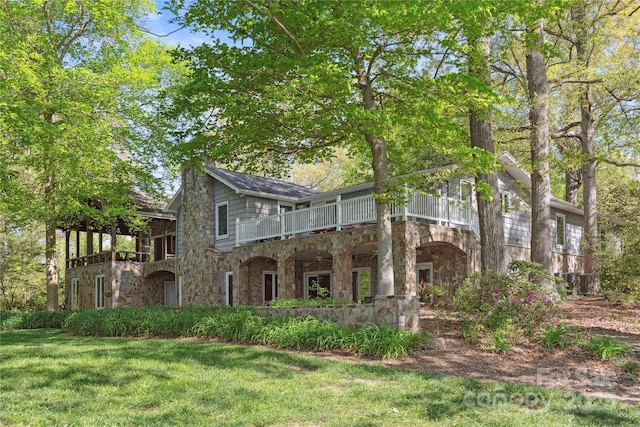 view of front of home featuring stone siding, a front yard, and a balcony