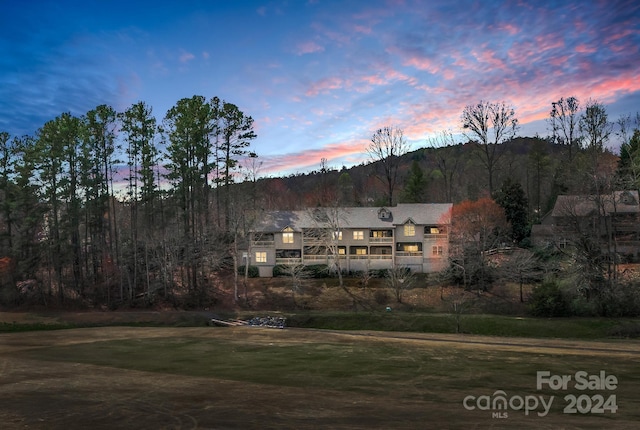 back house at dusk featuring a balcony and a yard