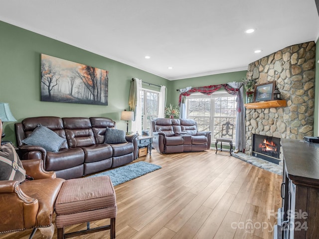 living room featuring light hardwood / wood-style flooring, ornamental molding, and a stone fireplace