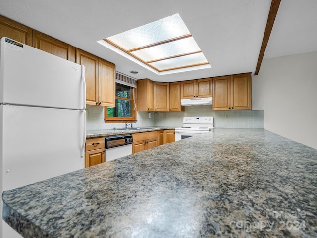 kitchen with a skylight, white appliances, and backsplash