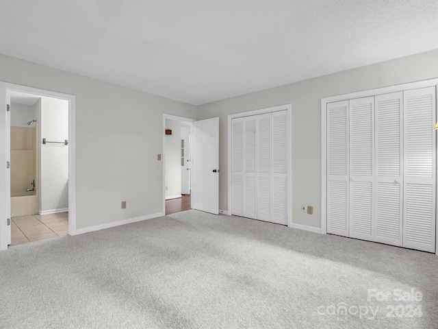 unfurnished bedroom featuring ensuite bath, light carpet, and two closets