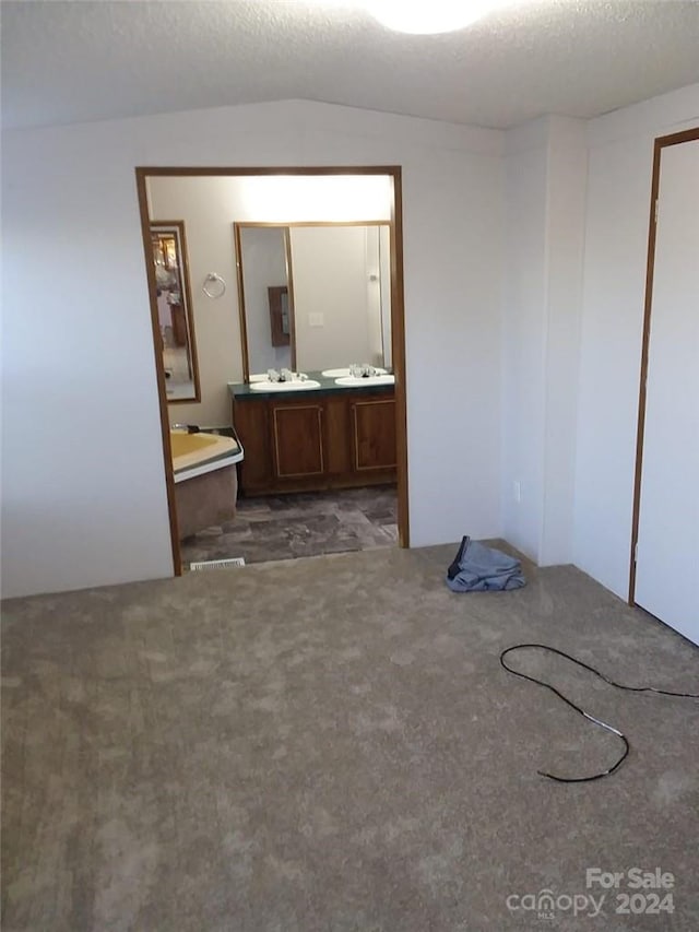 interior space featuring a textured ceiling, sink, dark colored carpet, and lofted ceiling