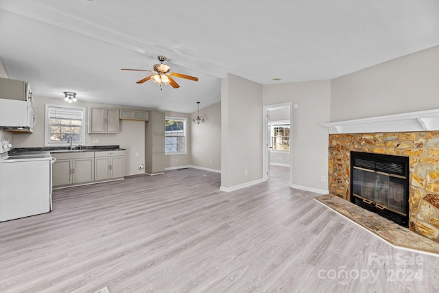 unfurnished living room featuring sink, ceiling fan, light hardwood / wood-style floors, a stone fireplace, and vaulted ceiling