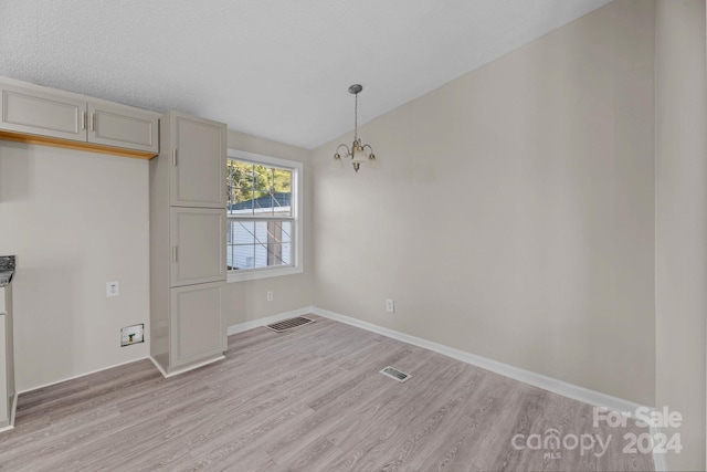 unfurnished dining area featuring lofted ceiling, a chandelier, and light hardwood / wood-style flooring