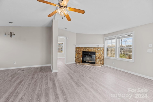 unfurnished living room featuring a stone fireplace, ceiling fan with notable chandelier, and light wood-type flooring