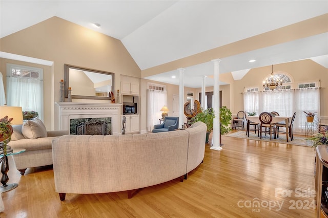 living room with a high end fireplace, decorative columns, high vaulted ceiling, an inviting chandelier, and light wood-type flooring