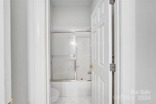 bathroom featuring tile floors, toilet, and bath / shower combo with glass door