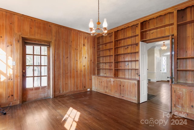 spare room featuring a healthy amount of sunlight, wood walls, dark wood-type flooring, and a notable chandelier