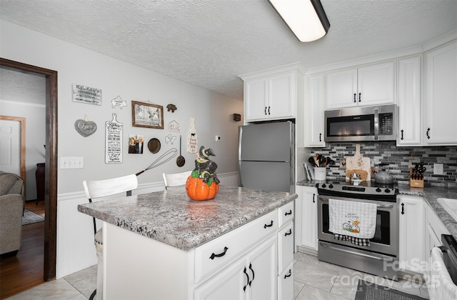 kitchen featuring appliances with stainless steel finishes, backsplash, a kitchen island, stone countertops, and white cabinetry