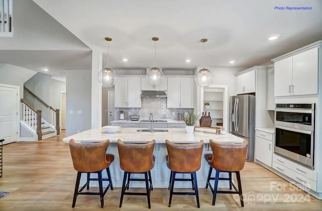 kitchen with white cabinets, a center island with sink, decorative light fixtures, and light hardwood / wood-style flooring