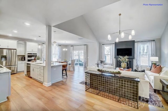 living room featuring a chandelier, vaulted ceiling, light wood-type flooring, and sink