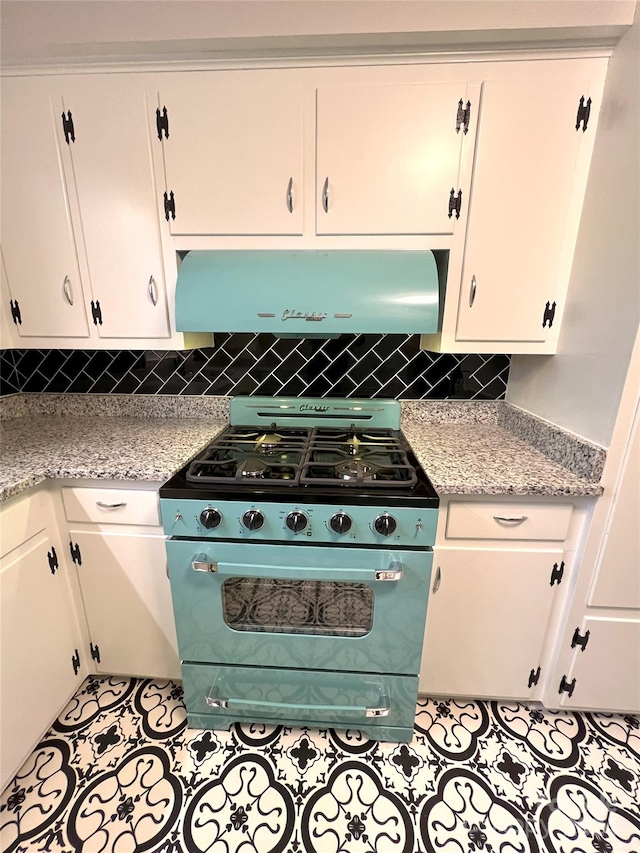 kitchen featuring white cabinetry, premium stove, light stone countertops, backsplash, and wall chimney range hood