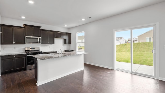 kitchen featuring a wealth of natural light, dark hardwood / wood-style flooring, stainless steel appliances, and a center island with sink