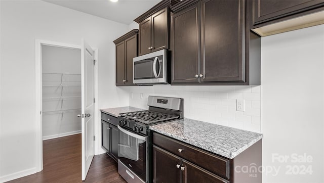 kitchen featuring appliances with stainless steel finishes, backsplash, dark hardwood / wood-style floors, light stone counters, and dark brown cabinetry