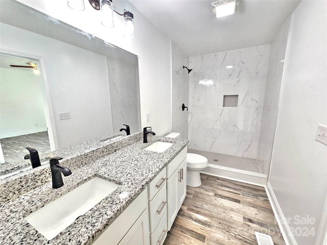 bathroom featuring double vanity, a tile shower, toilet, ceiling fan, and wood-type flooring