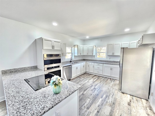 kitchen with appliances with stainless steel finishes, white cabinetry, light stone countertops, and light hardwood / wood-style flooring