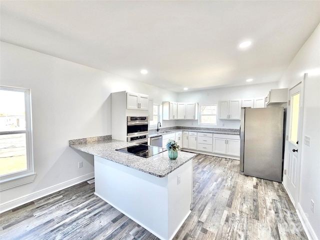 kitchen with kitchen peninsula, white cabinetry, light wood-type flooring, stainless steel appliances, and light stone counters